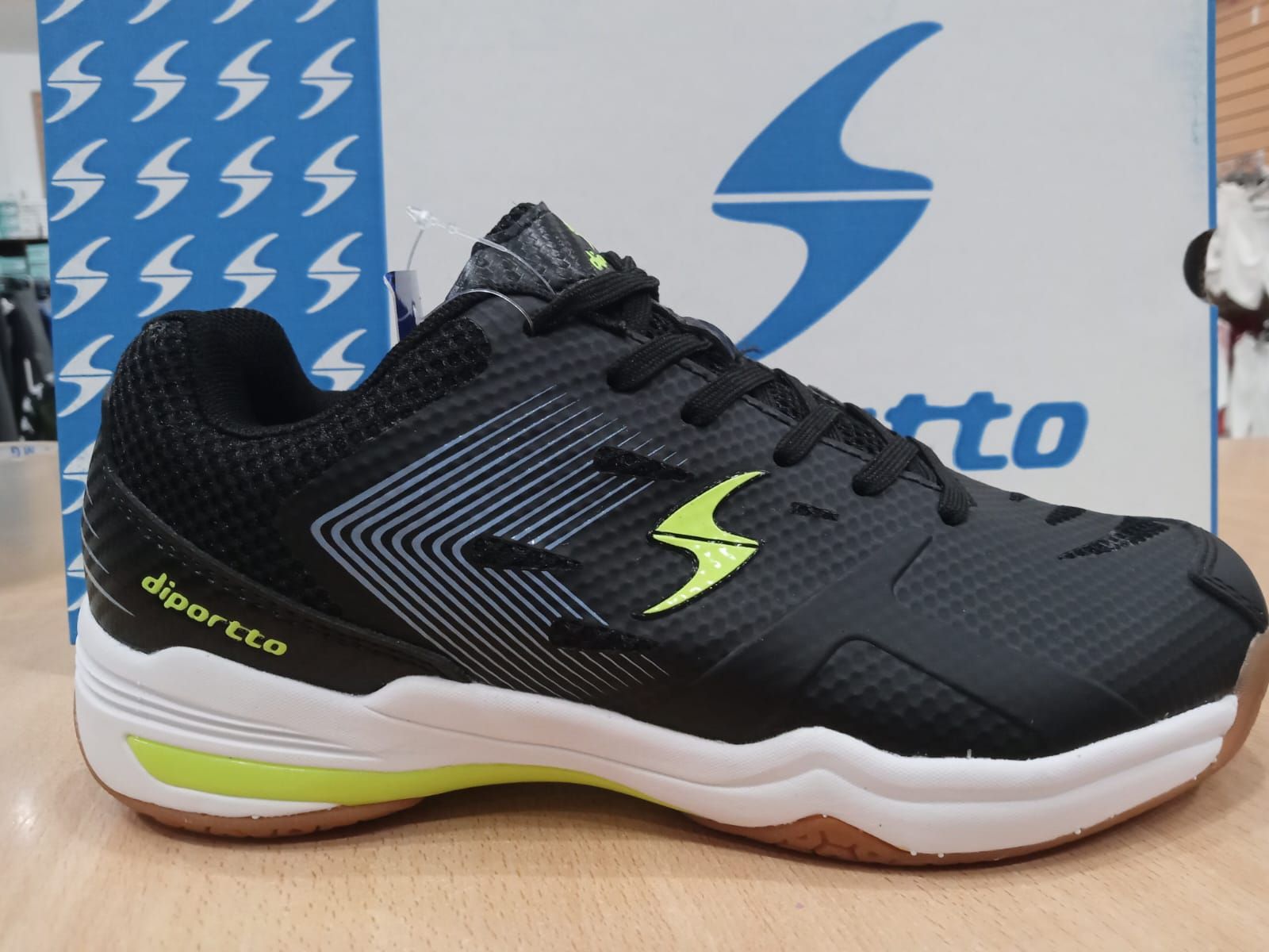 Zapatillas deportivas negras con detalles en verde neón y suela blanca, vistas de perfil sobre un fondo de caja de marca.