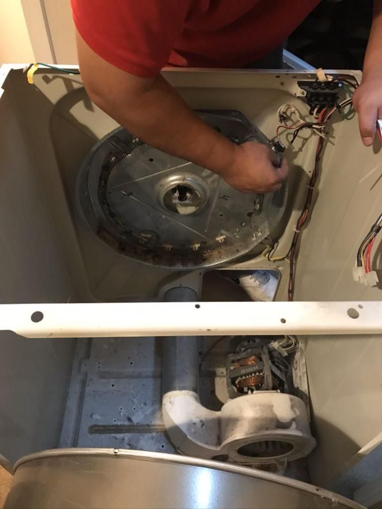 A man is working on the inside of a washing machine.