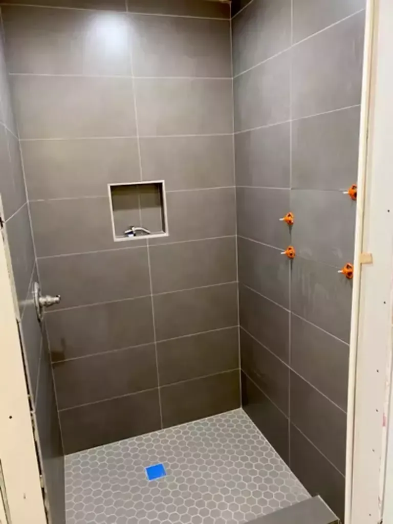 A shower stall with gray tiles and a blue drain.