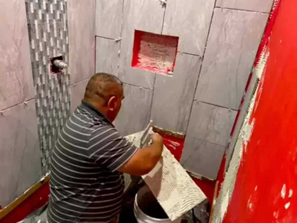 A man is laying tiles in a bathroom.