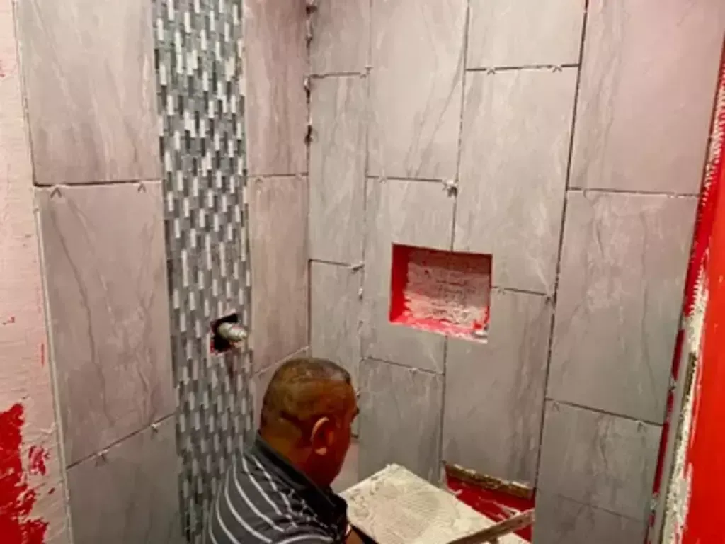 A man is laying tiles in a bathroom.