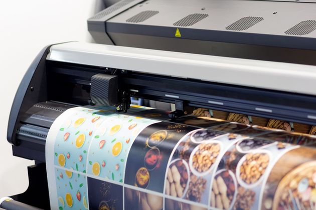 A vinyl printer cutting a roll of printed adhesive stickers featuring various food and pattern designs.