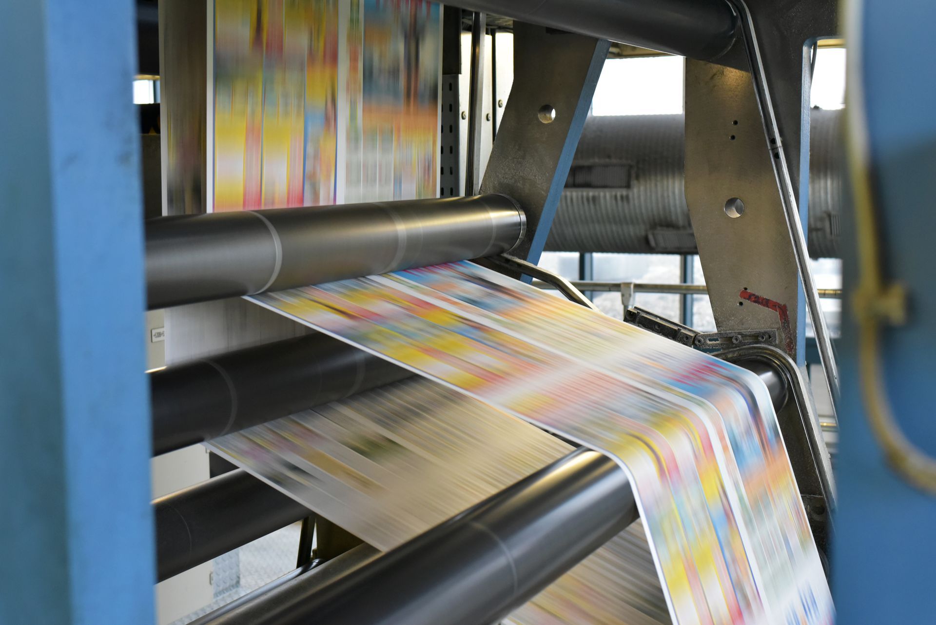 A long, colorful strip of printed material passes through the rollers of an industrial offset printing press.