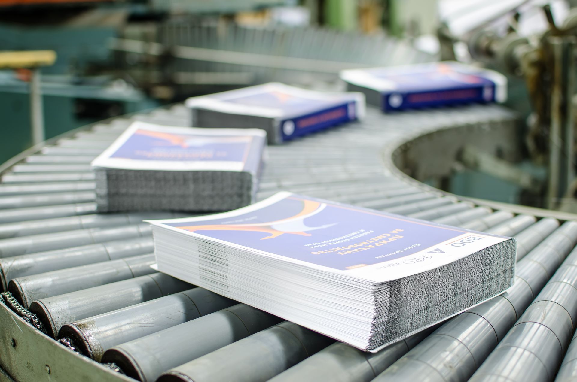 Stacks of printed books moving along an industrial conveyor belt in a printing facility.