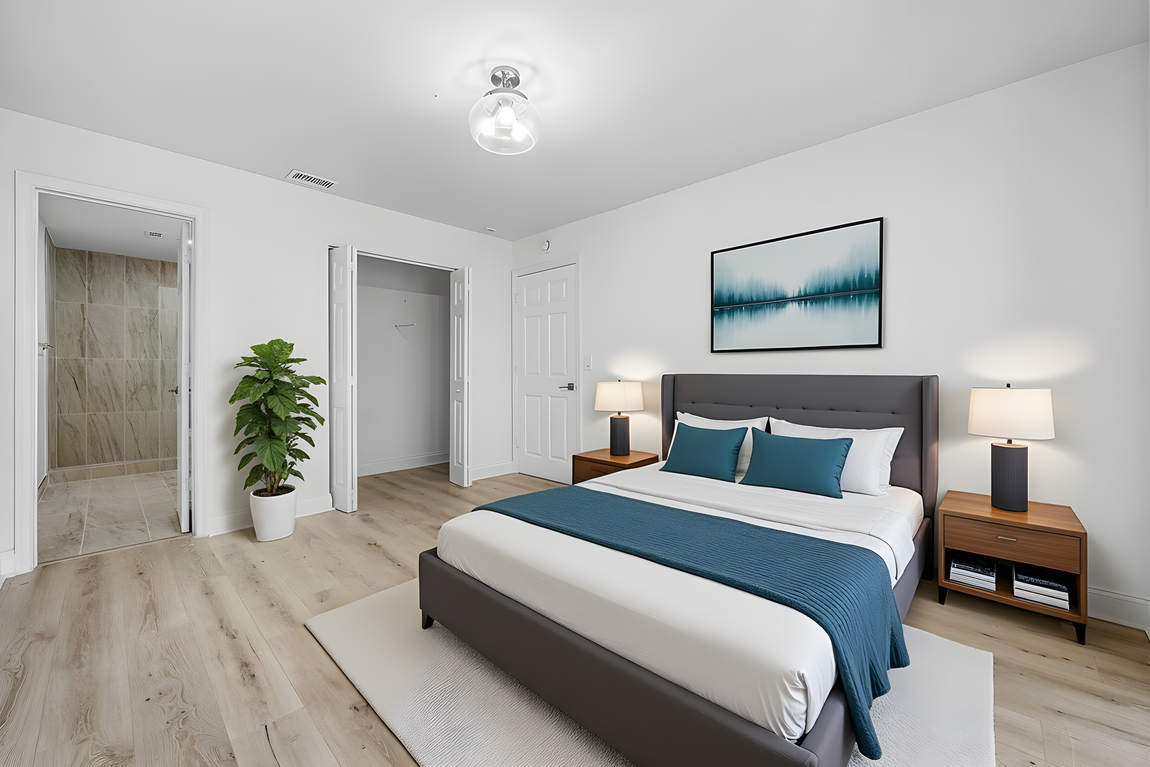 Modern bedroom featuring a gray bed with blue bedding, wood-toned nightstands, a large green plant, and white walls.