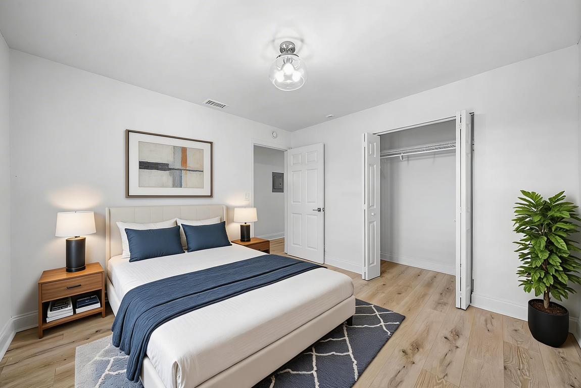 A minimalist bedroom with a bed featuring a white comforter and blue runner, two lamps, a closet, and a potted plant.