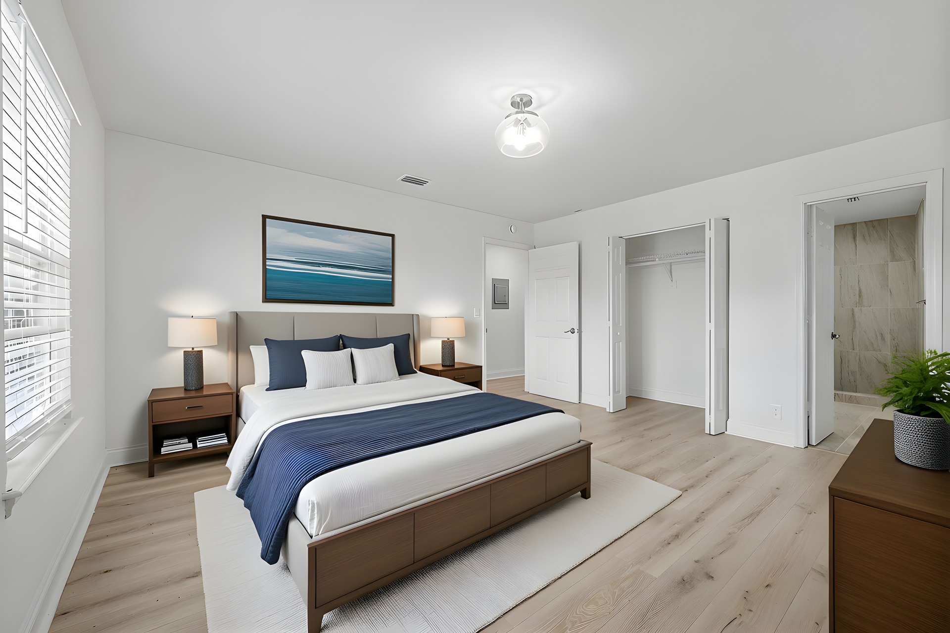 A bright, modern bedroom featuring a queen bed with blue bedding, light wood floors, a closet, and a doorway to a bathroom.