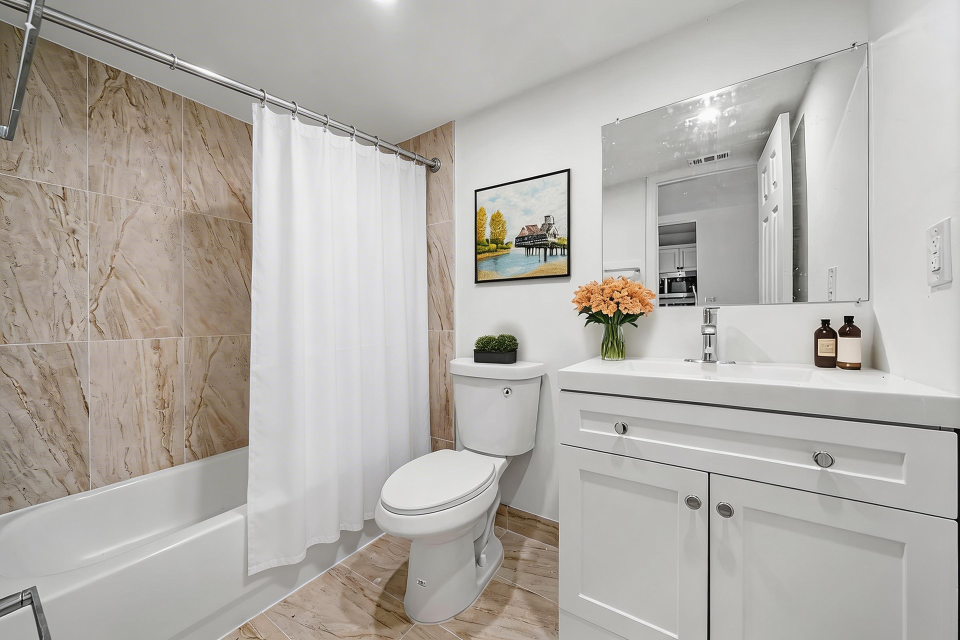 A bright bathroom featuring a white vanity, a toilet, and a bathtub with marble-look tile walls and a white curtain.