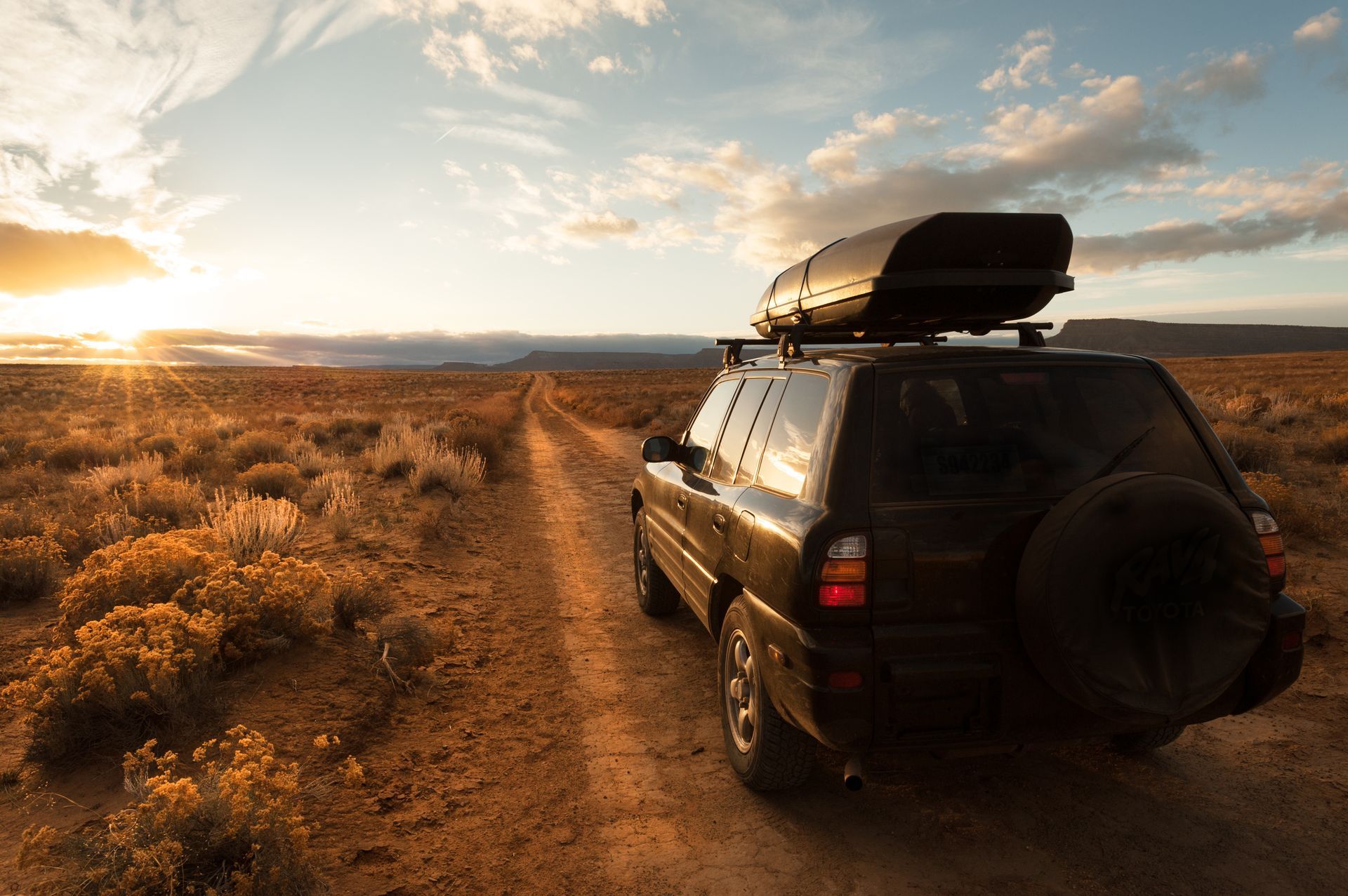 A black SUV with a roof rack is driving down a dirt road  | Gemba Automotive