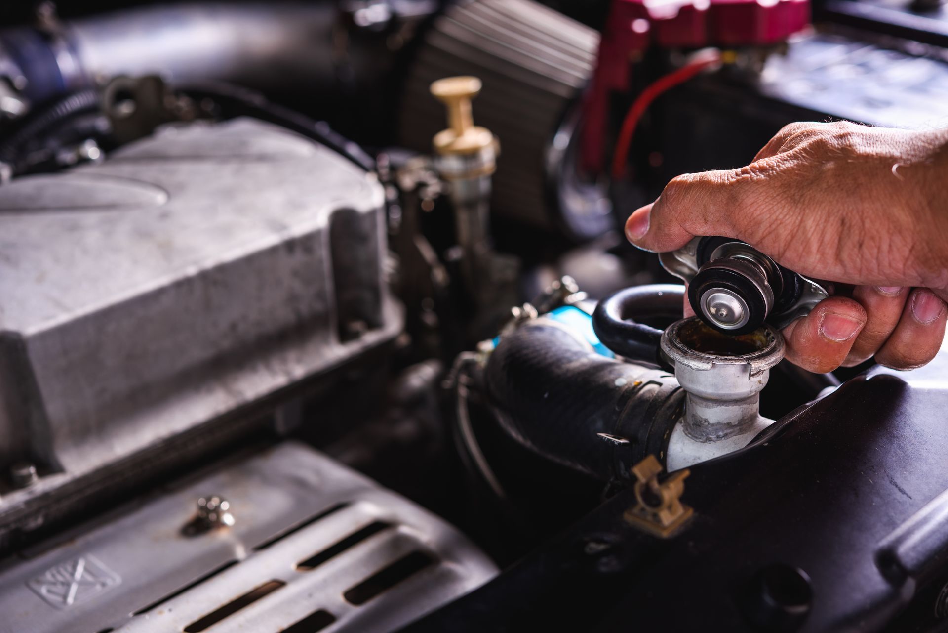 A person is opening a radiator cap on a car engine | Gemba Automotive