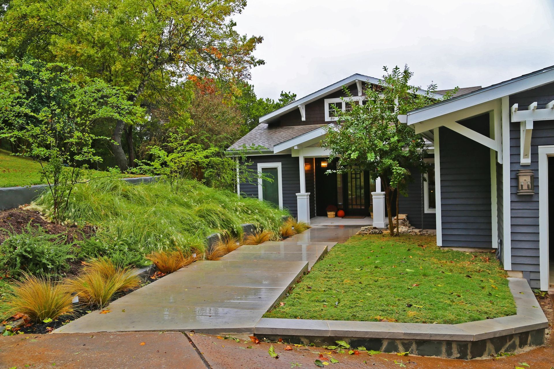 Dark gray house with white trim, a walkway, and landscaped yard. Overcast sky.