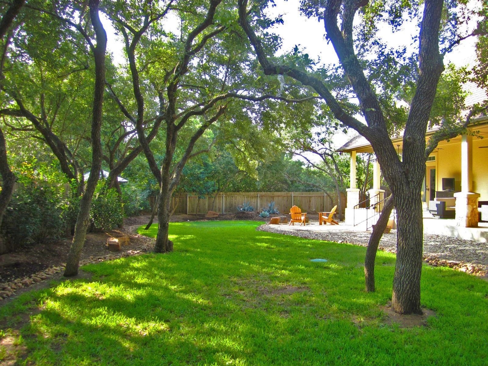 Green lawn shaded by trees, leading to a patio with seating.
