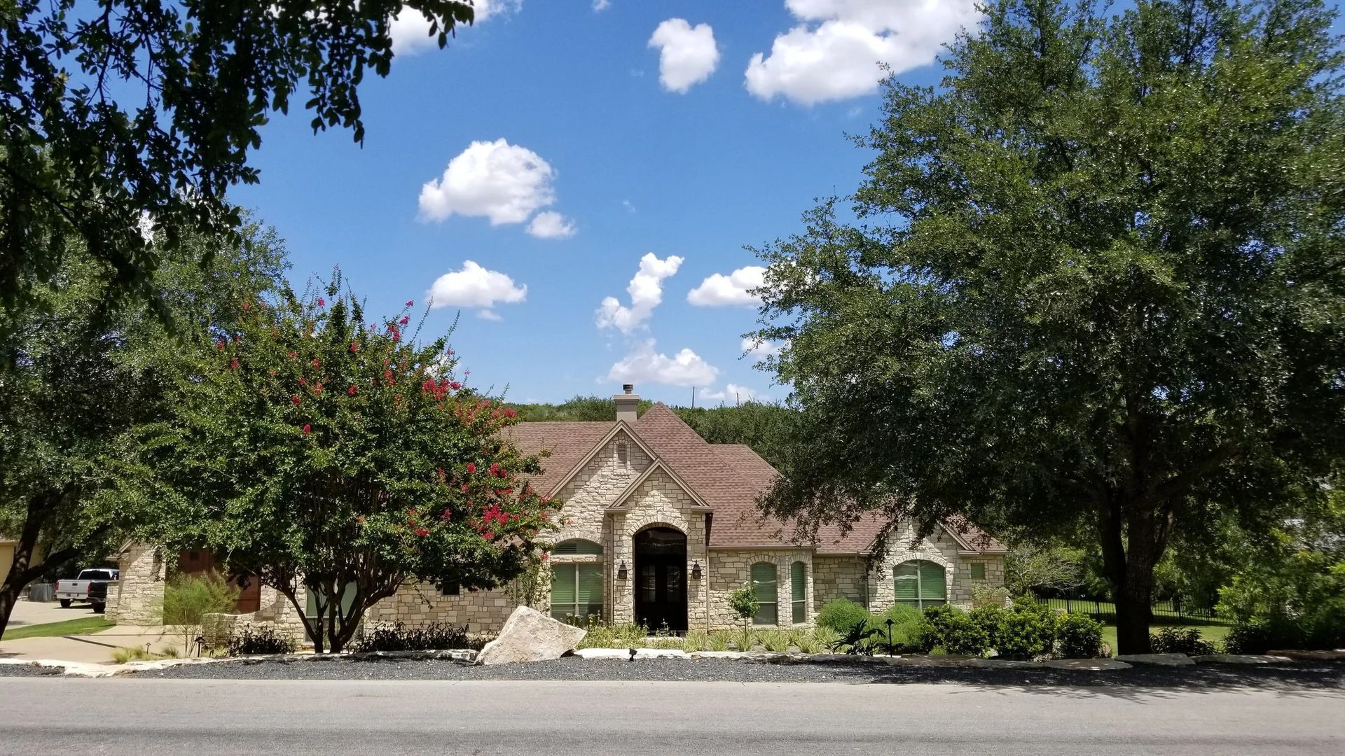 Stone house with a brown roof and green foliage under a blue sky with fluffy white clouds.