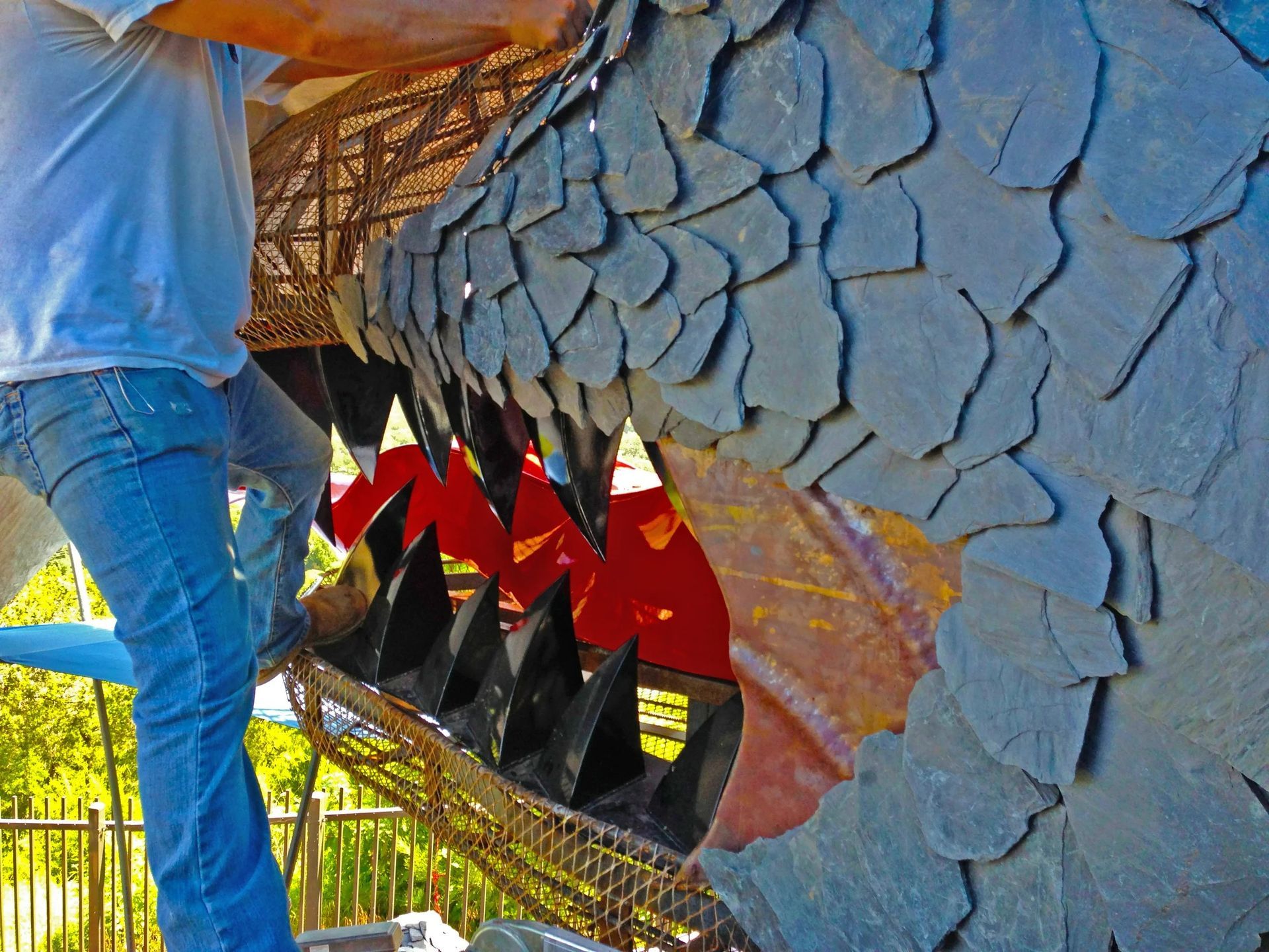 Person attaching dark stone scales to a dragon head sculpture.
