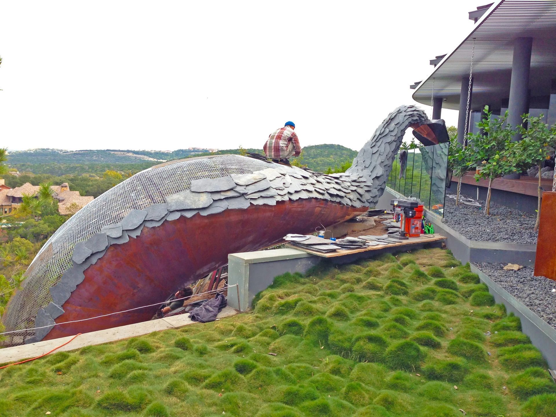 Large sculpture of a whale emerging from a hillside with a person working on top.