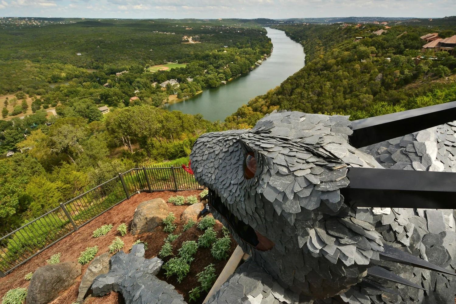 Dragon sculpture overlooking a river valley. Green trees and blue sky.