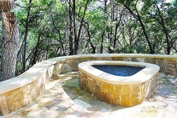 Triangular stone hot tub in a natural setting, surrounded by stone walls and trees.