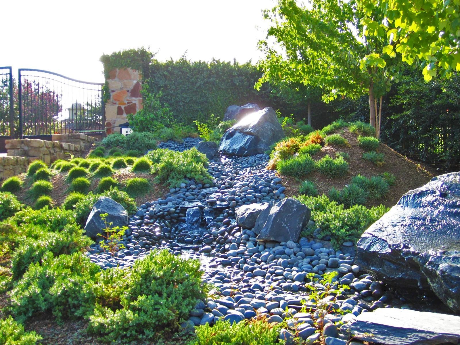 Landscaped water feature with a flowing stream of water, surrounded by rocks and greenery.
