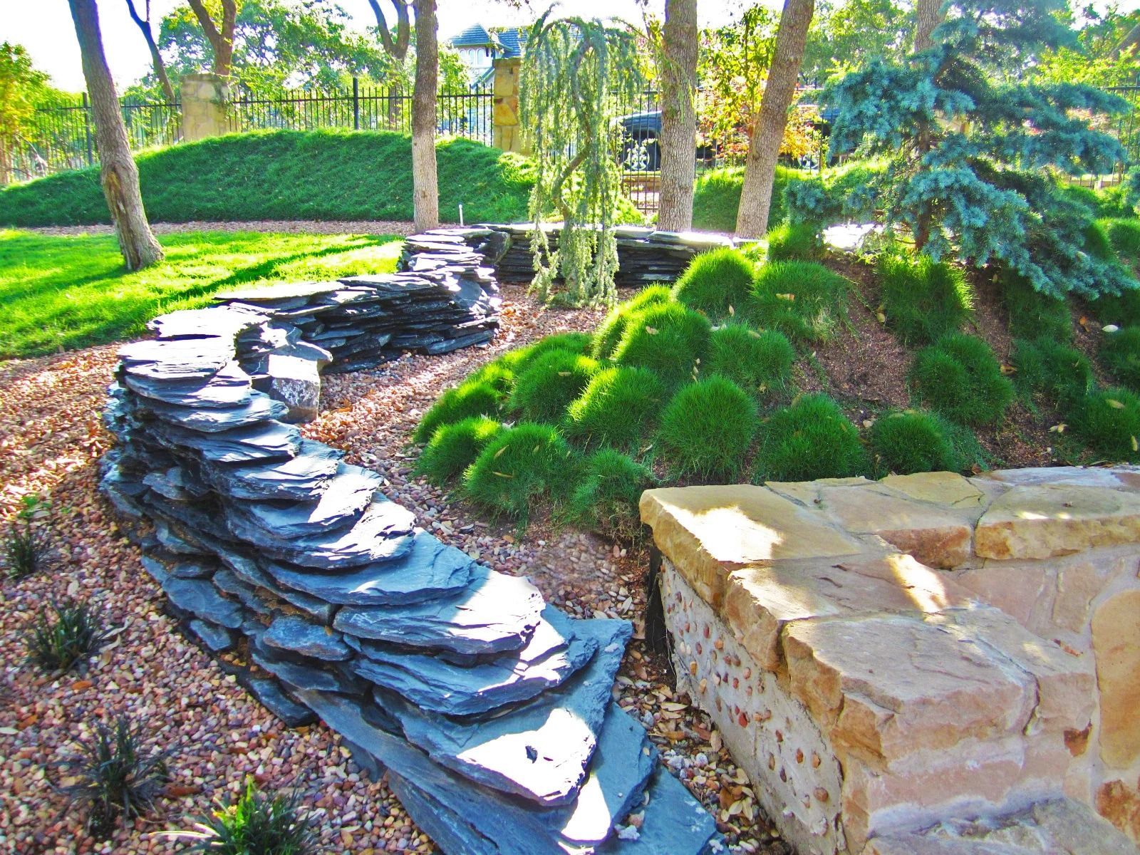 Stone retaining walls in a landscaped yard with green plants and trees.