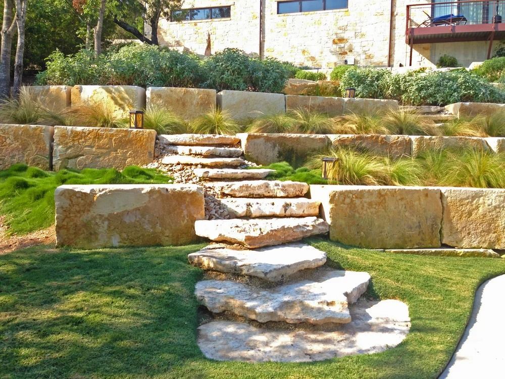 Stone steps cascade down a tiered landscape with grass and large stone retaining walls.