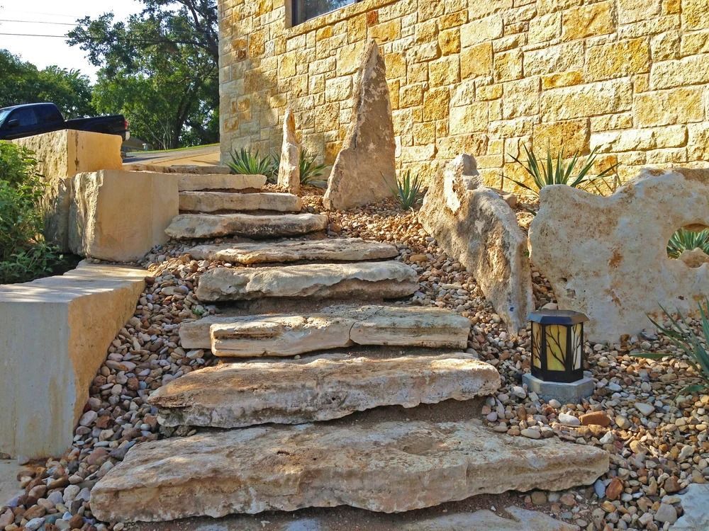Stone steps leading up to a beige stone building, surrounded by gravel and plants, illuminated by a small lantern.