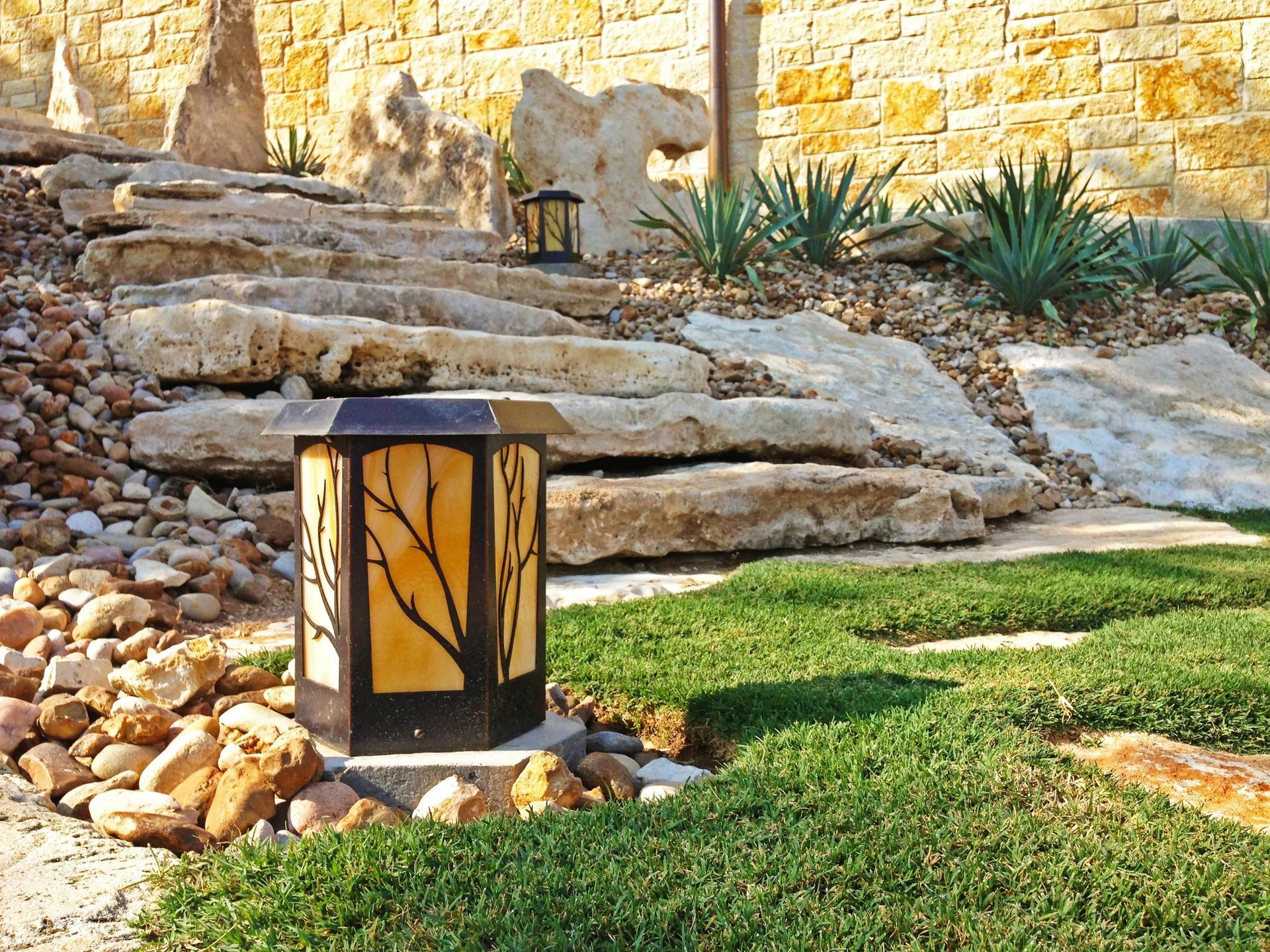 Stone steps in a landscaped yard with a decorative lantern. Green grass and rock features are present.