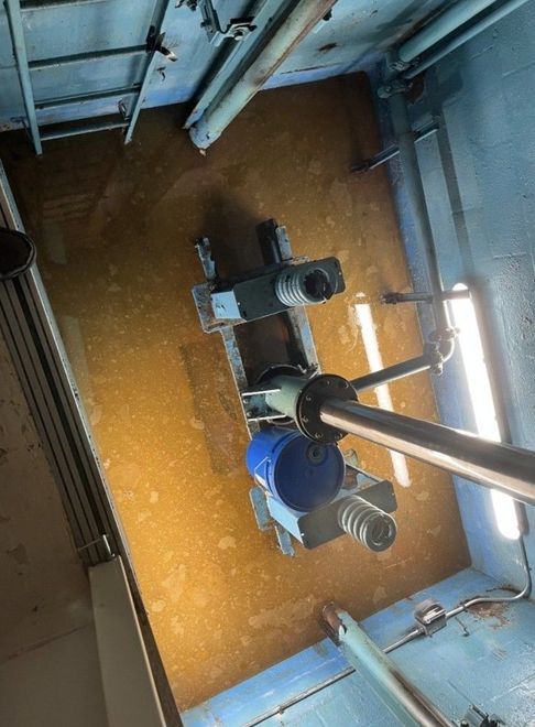 Blue industrial machine in a metal tank of brown liquid, viewed from above.