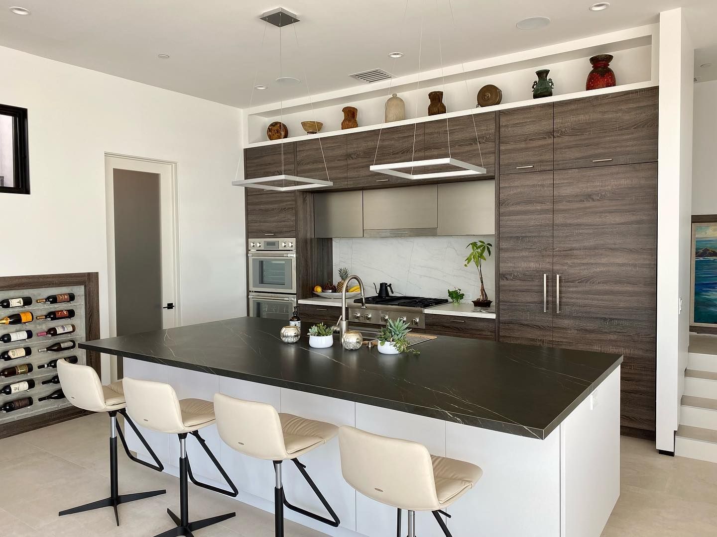 Modern kitchen with a large island, four white stools, wood cabinets, and stainless steel appliances