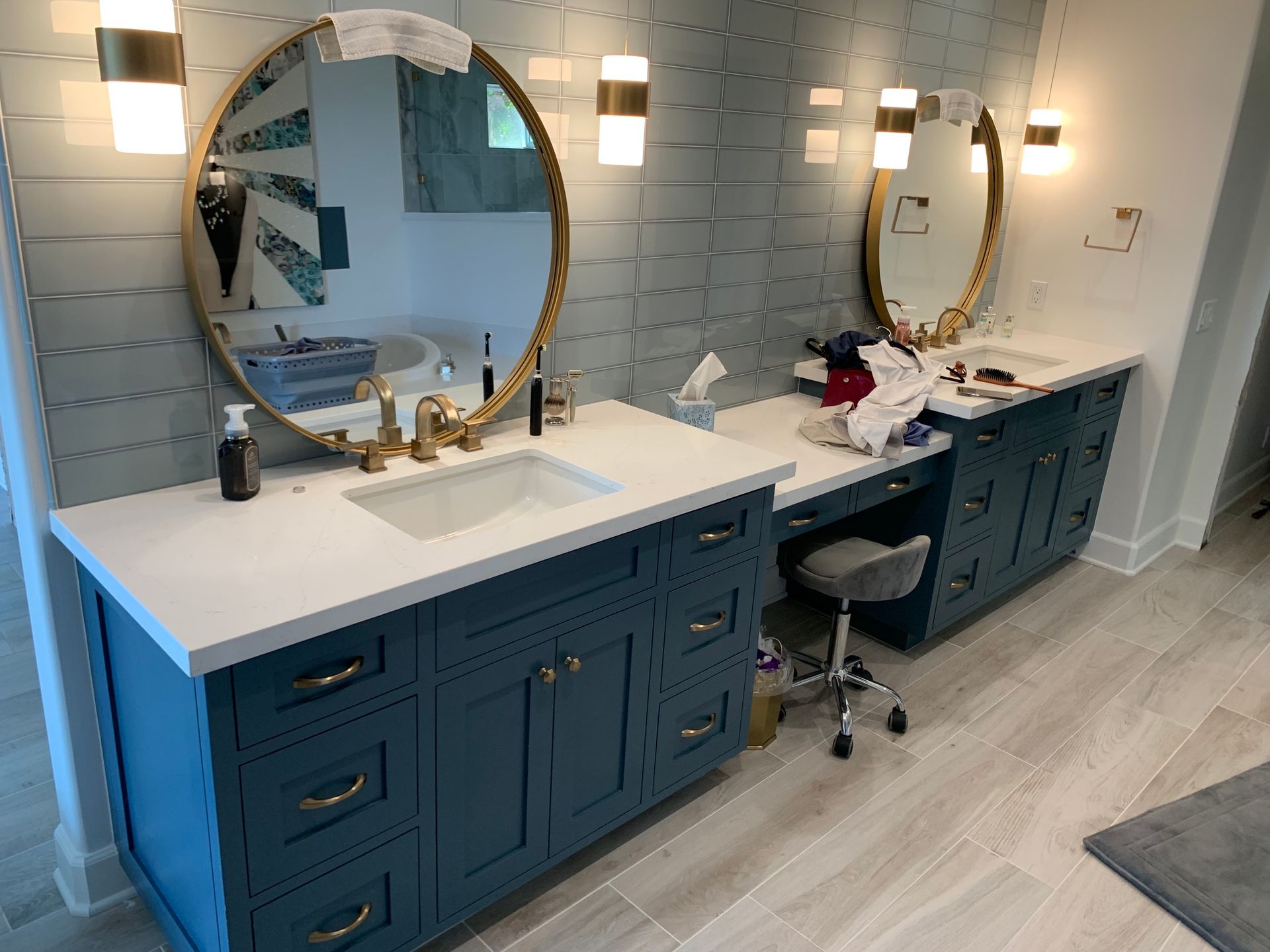 Double vanity bathroom with blue cabinets, round mirrors, and a stool between sinks