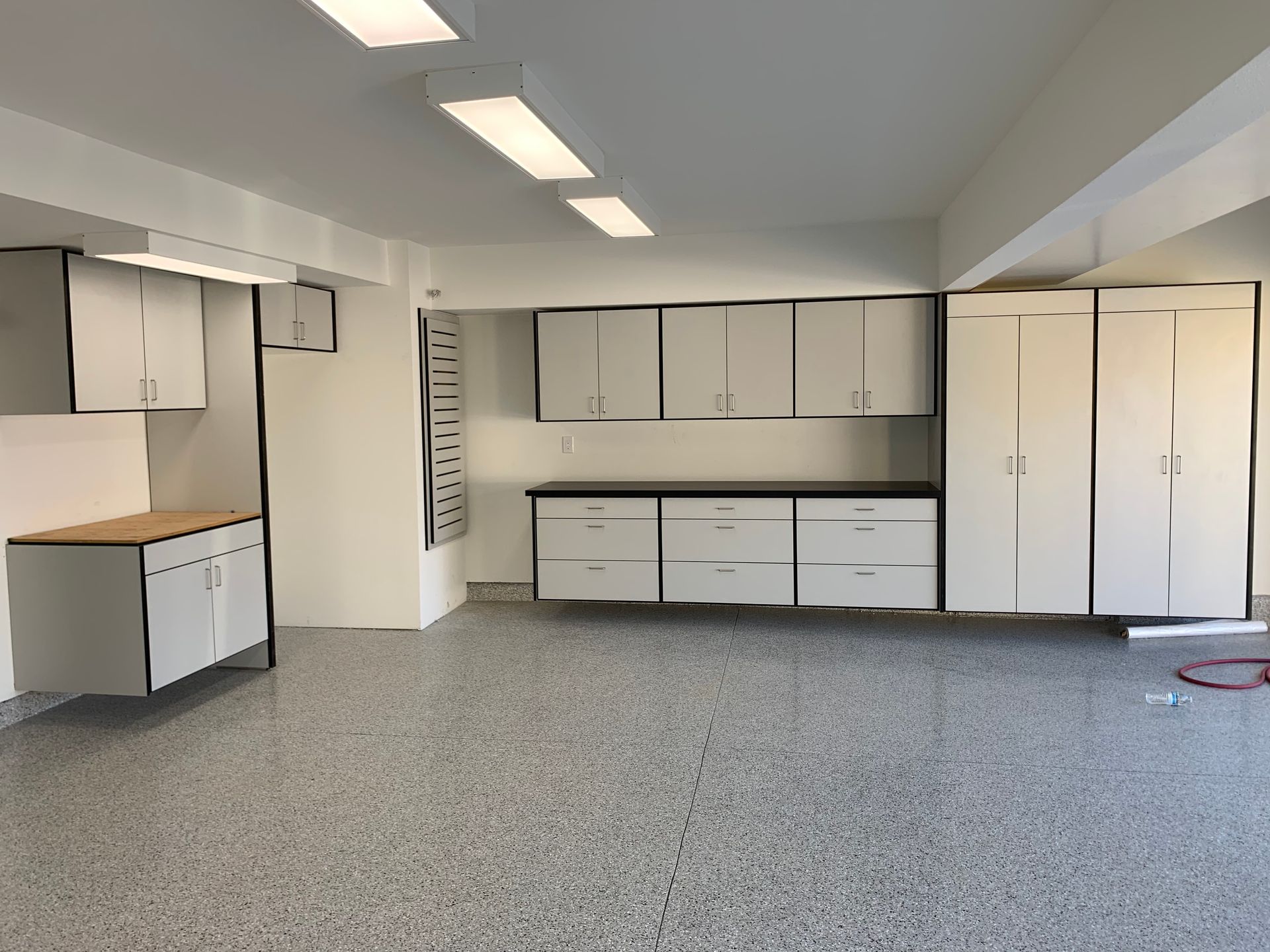 Empty garage with white cabinets, gray carpet, and built-in storage along the walls
