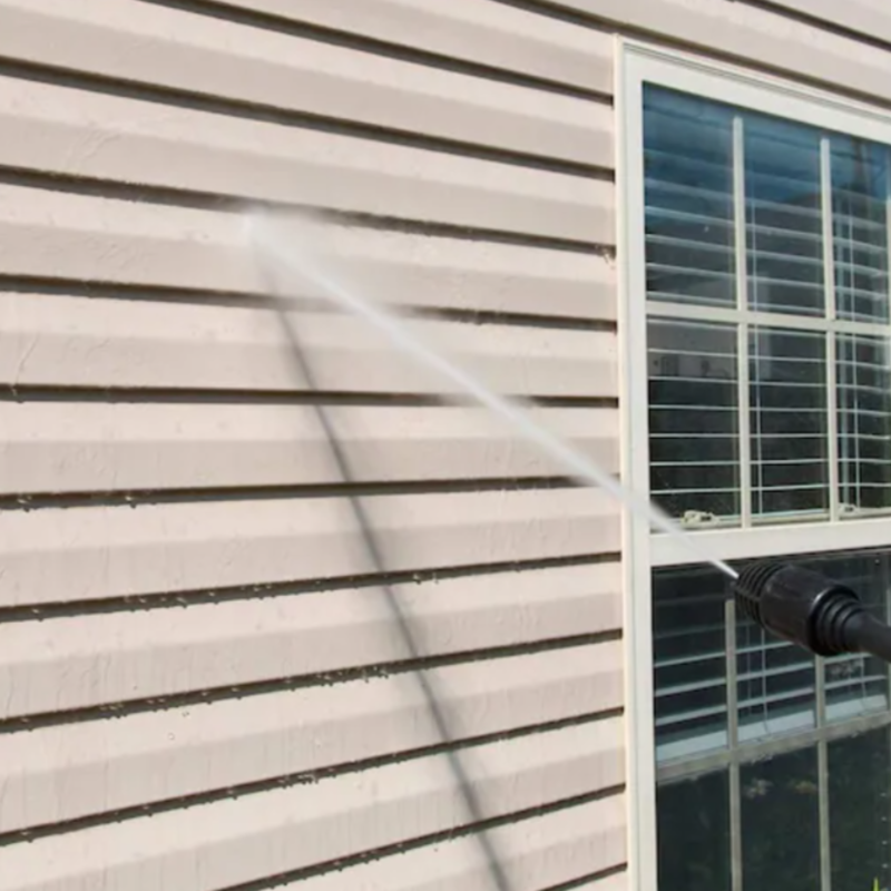 A person is cleaning the side of a house with a high pressure washer.