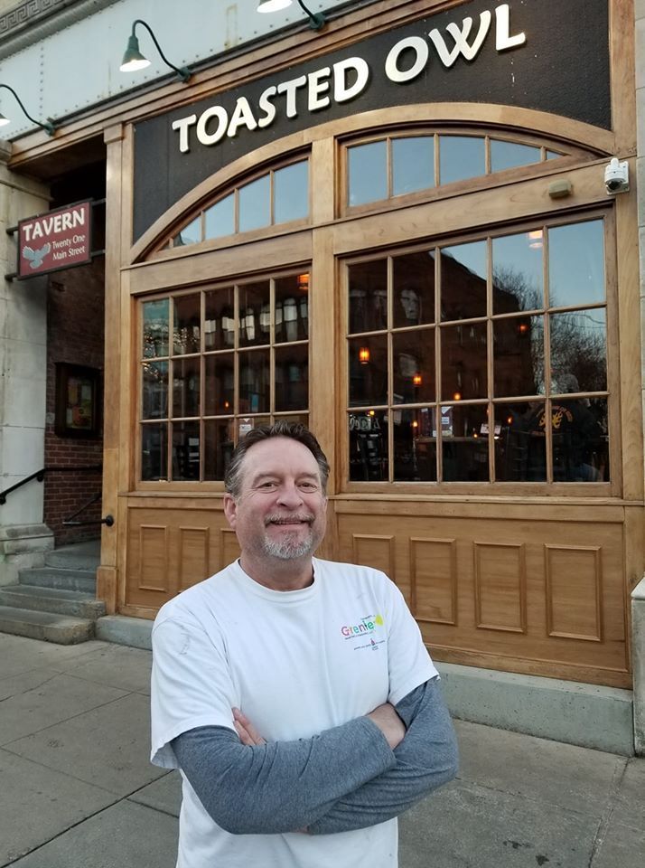 A man is standing in front of a toasted owl restaurant