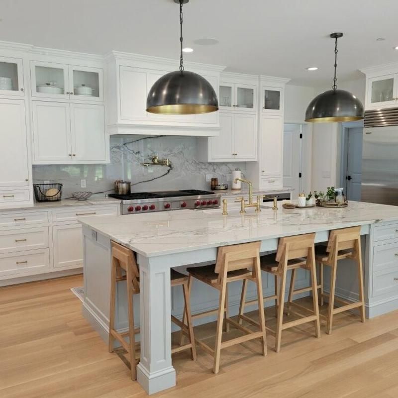 A kitchen with white cabinets , a large island , stools and a stove.