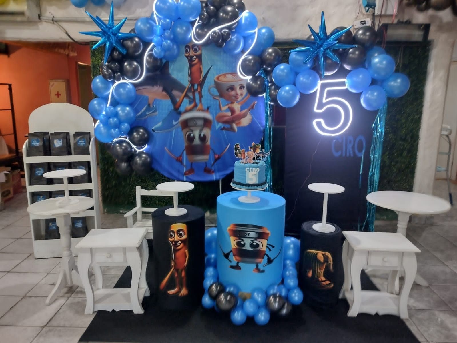 Decoración para fiesta de cumpleaños con globos azules y negros, pastel y adornos de personajes.