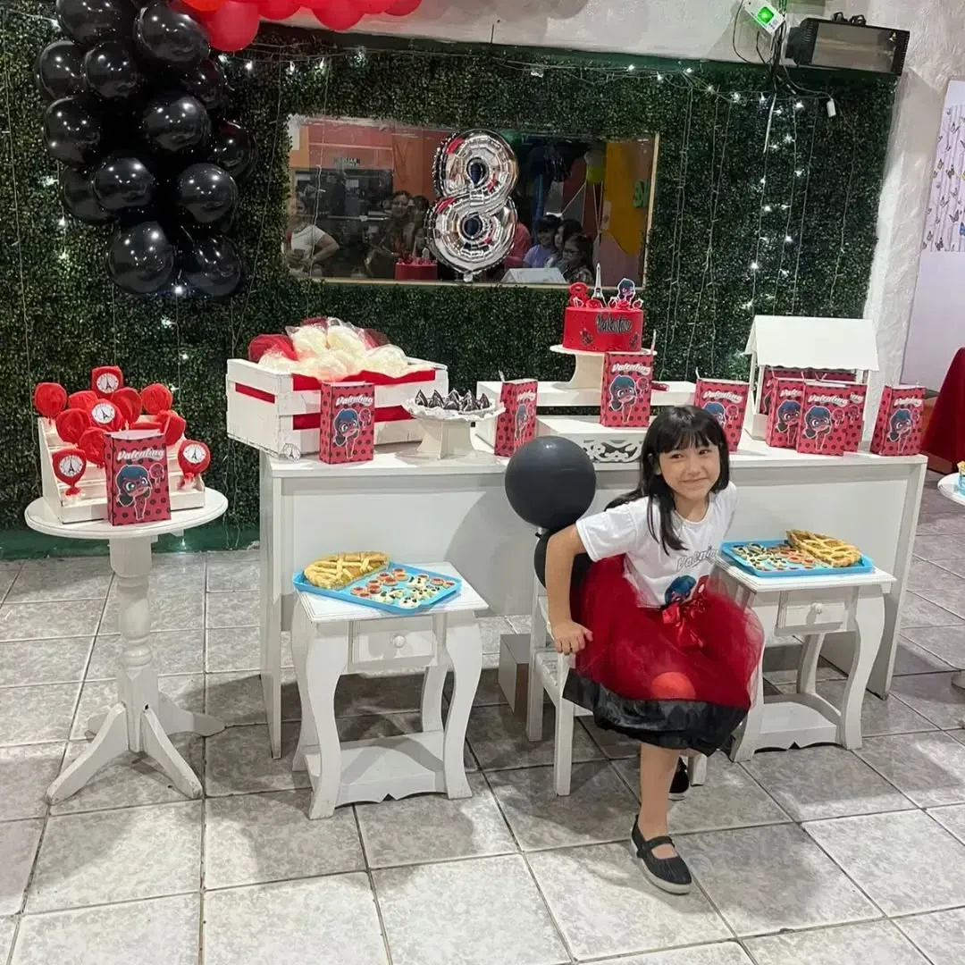 Una niña sonríe a la cámara en una fiesta de cumpleaños con decoración roja, negra y blanca.