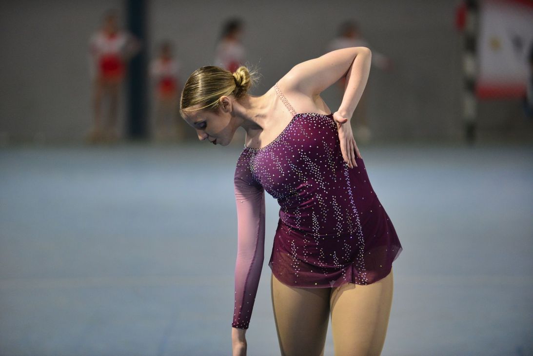 Una patinadora artística con un vestido morado brillante realiza su rutina