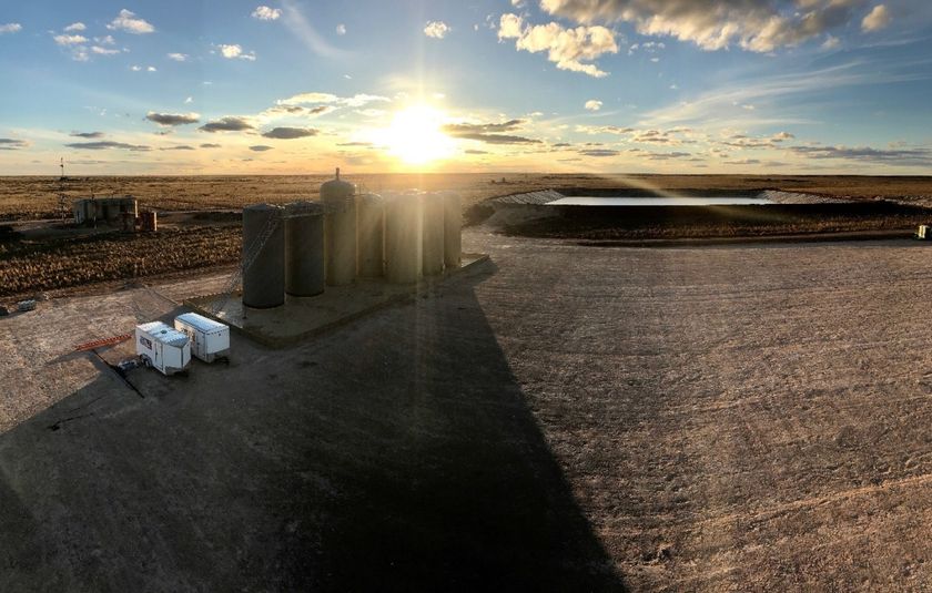 There is a sunset in the background and a shadow of a building on the ground.