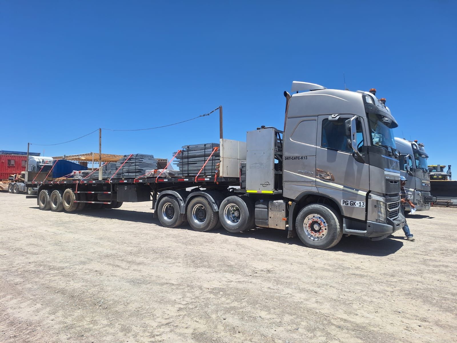 Camión que transporta contenedores de envío verdes en un remolque de plataforma, en un entorno al aire libre.