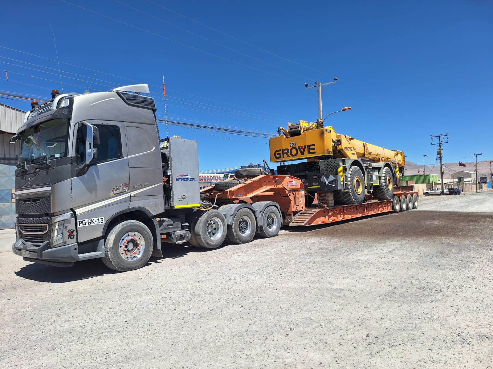 Un gran camión transporta una grúa amarilla sobre un remolque de plataforma, bajo un cielo azul claro.