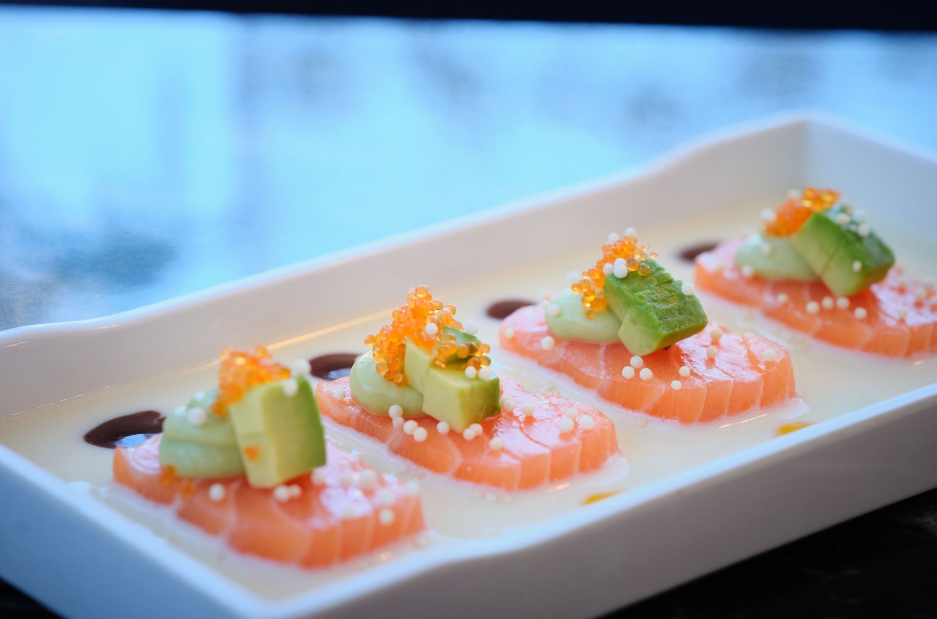 Un piatto bianco guarnito con salmone, avocado e caviale.