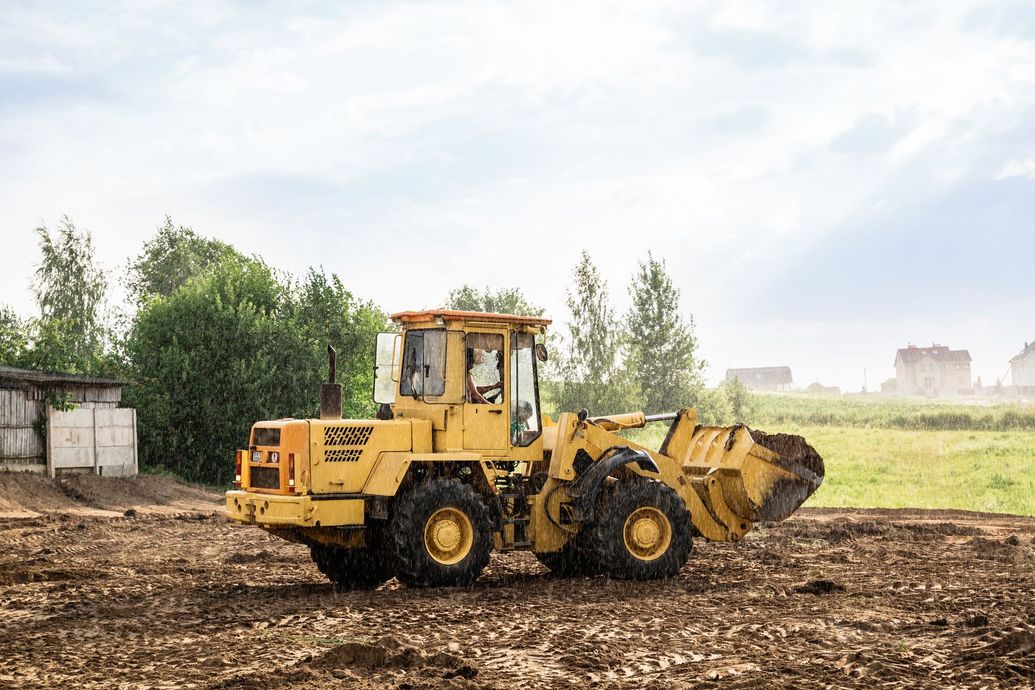 Yellow front loader on a dirt field under a cloudy sky