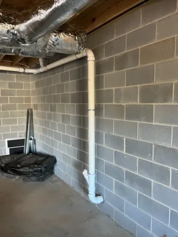 Basement interior with cinder block wall, plumbing pipes, and ductwork.