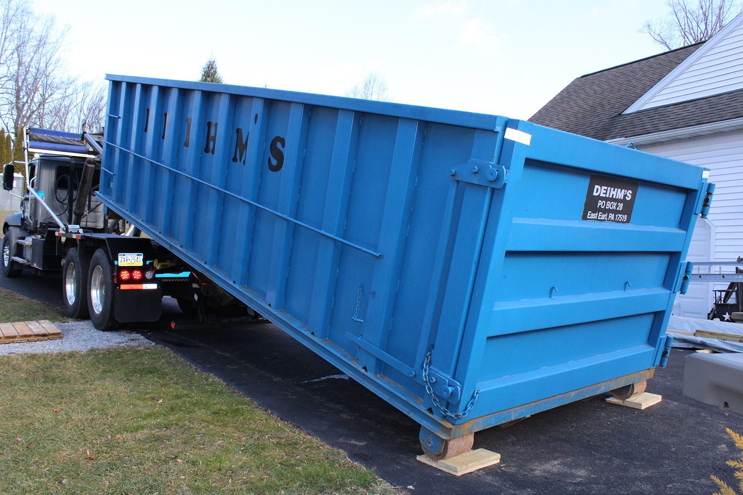 Deihm's Disposal of PA's blue dumpster is sitting on the side of a road next to a truck.