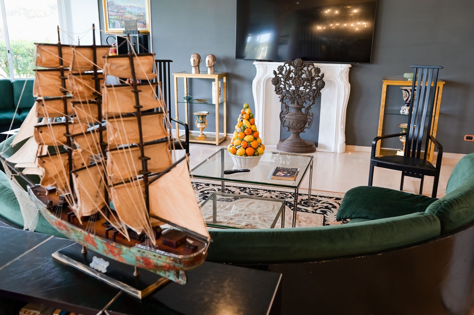 Esposizione di modellini di navi in una stanza con TV, sedia verde e scultura decorativa su un tavolo.