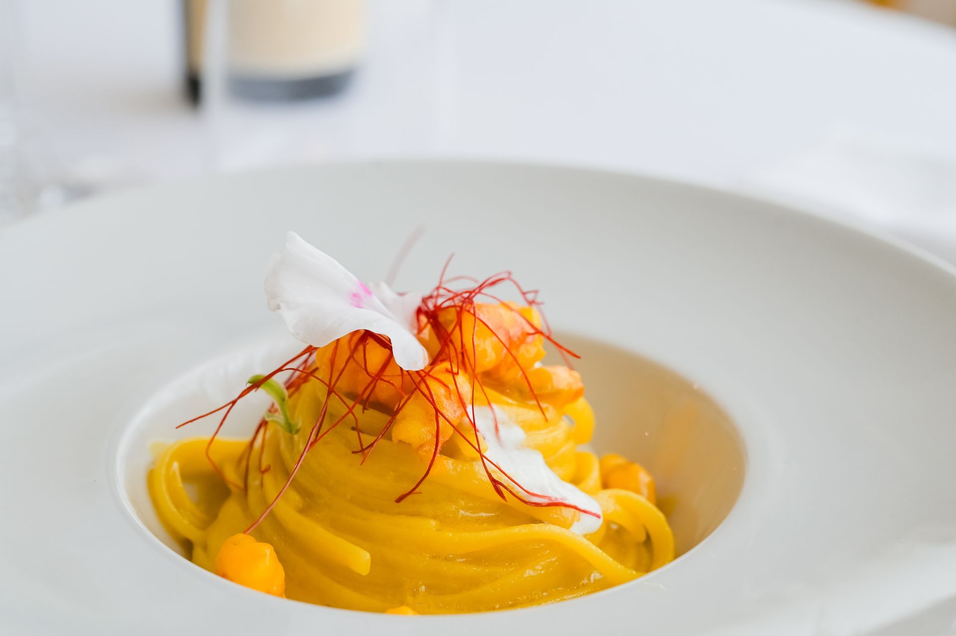 Pasta gialla in una ciotola bianca, guarnita con fili di zafferano e una decorazione bianca.