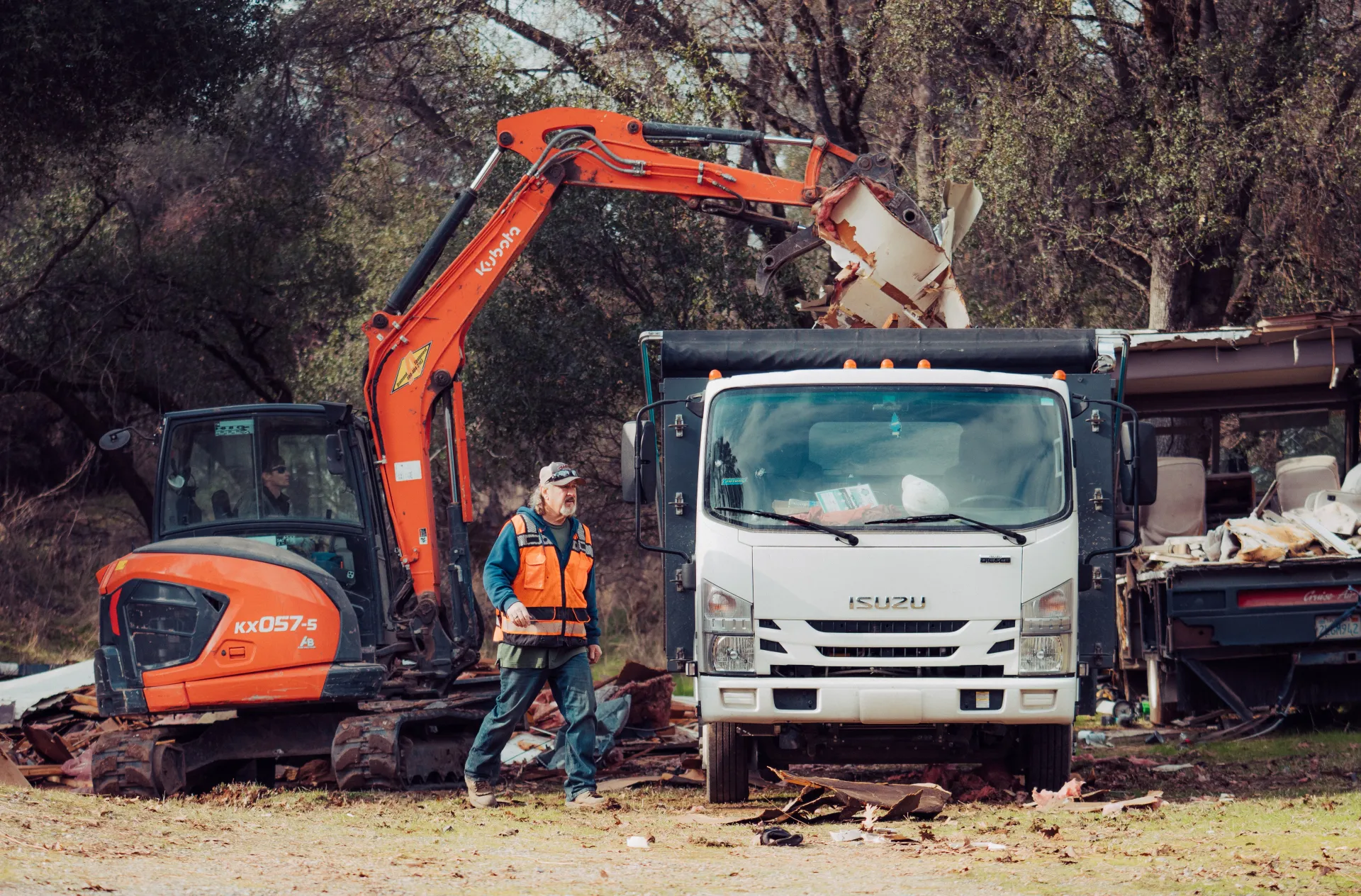 A man is standing next to an excavator and a dump truck.