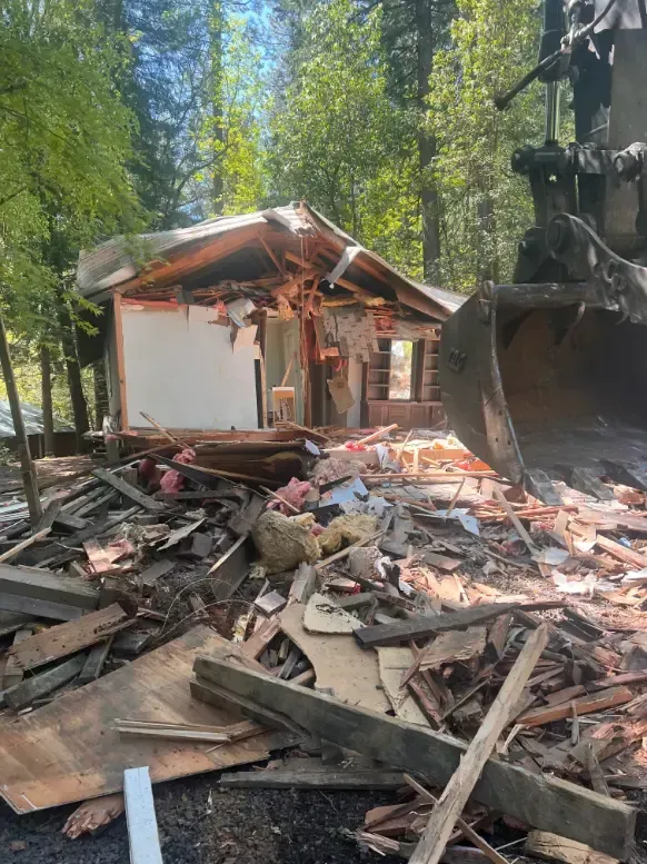 A house is being demolished by a excavatorr in the woods.