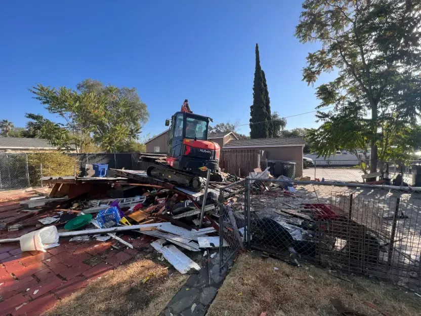 A bulldozer is demolishing a house in a backyard.