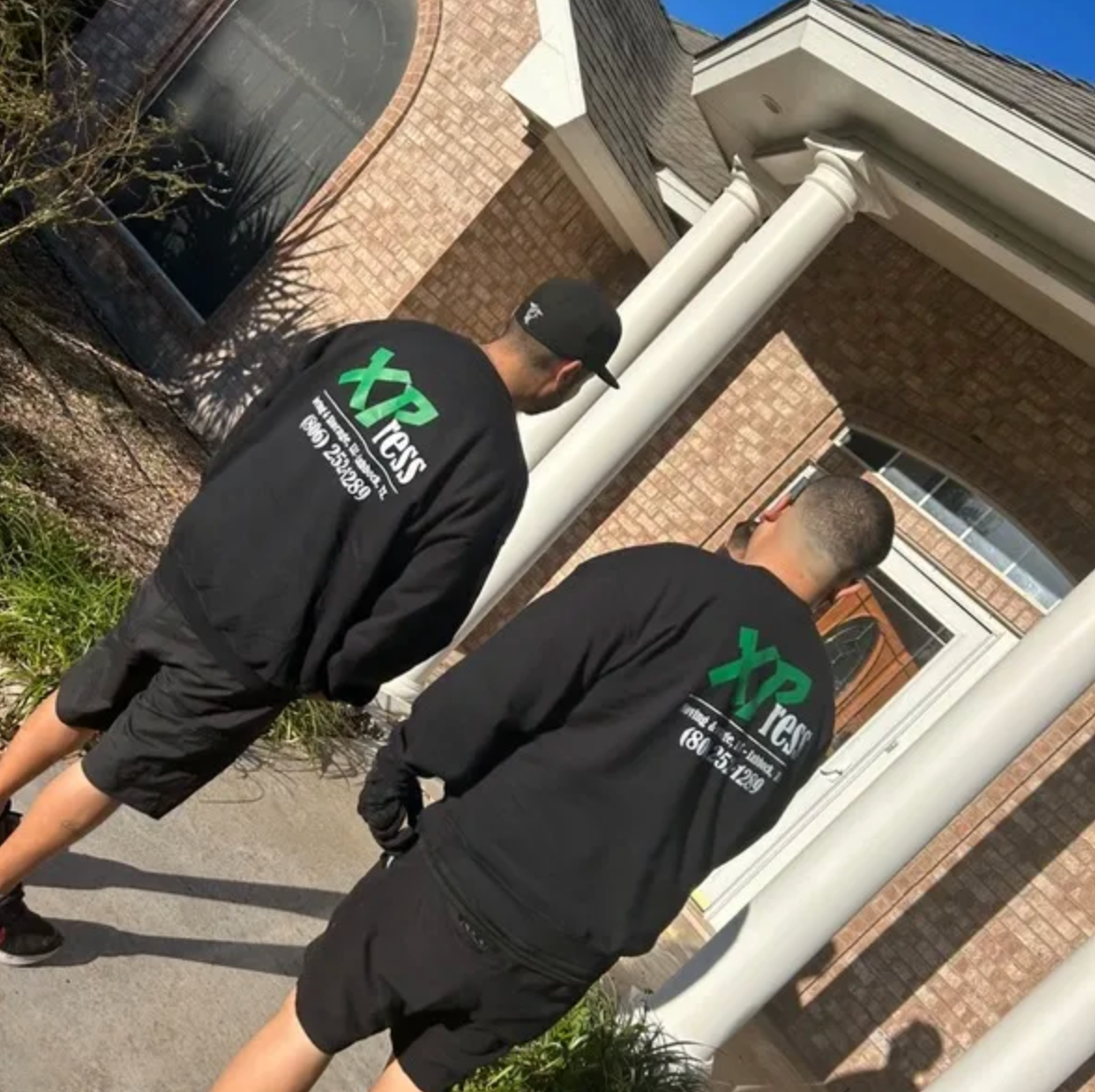 Two men wearing xpress shirts are standing in front of a house