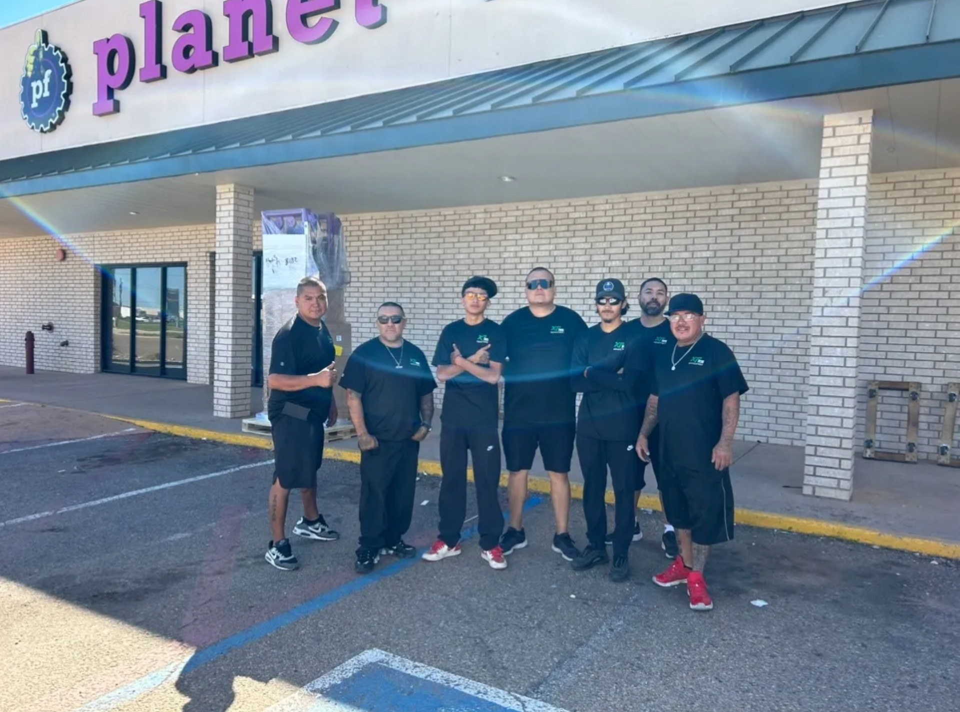 A group of men are posing for a picture in front of a planet fitness store.